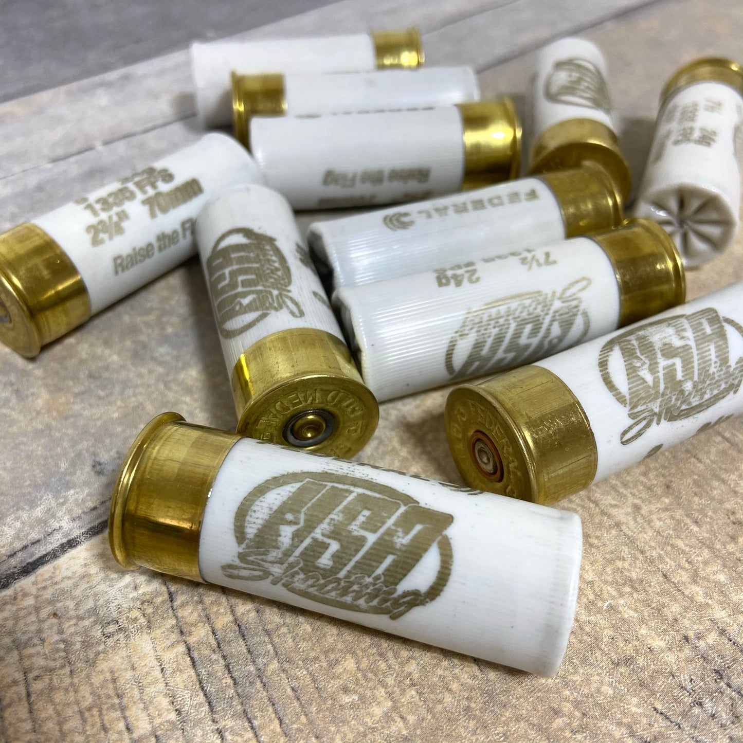 White used dummy rounds piled together on a rustic wood surface, with gold brass bases and various brand markings.