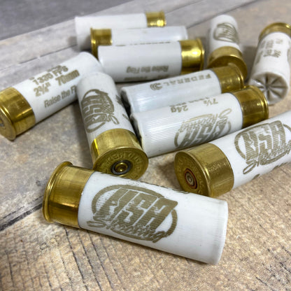 White used dummy rounds piled together on a rustic wood surface, with gold brass bases and various brand markings.