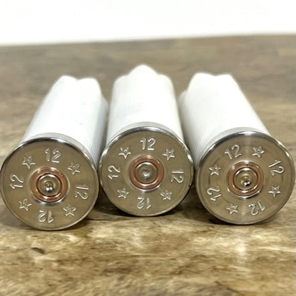 Three white used shotshells lying on their sides showing headstamps stamped 12 with stars and a copper primer