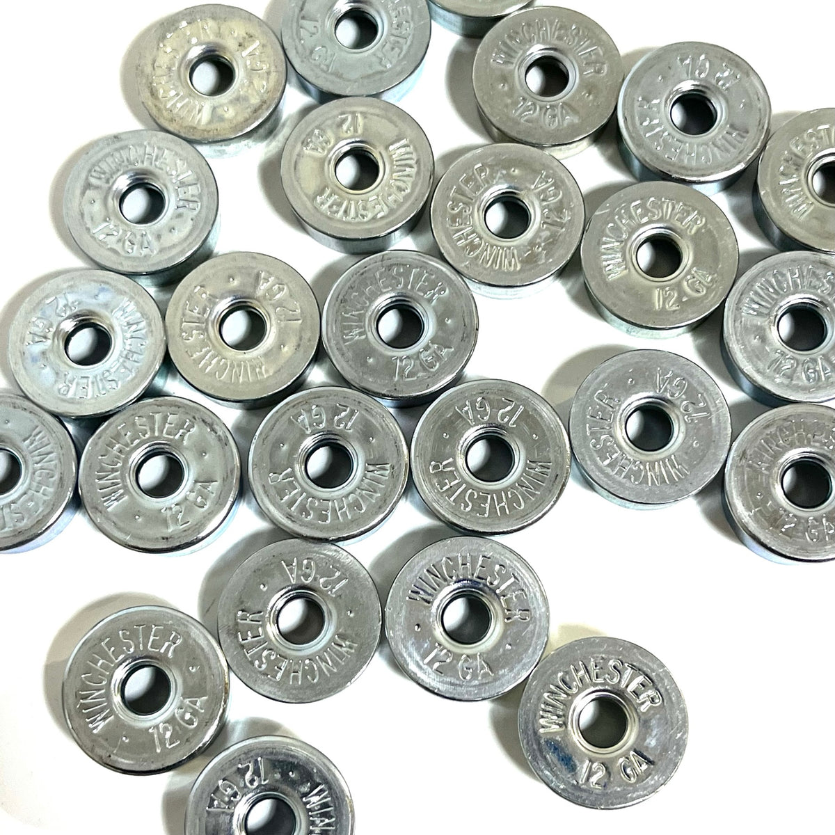 Many silver Winchester 12 gauge deprimed shotgun shell steel bottoms with the primer removed, viewed from above showing an open hole