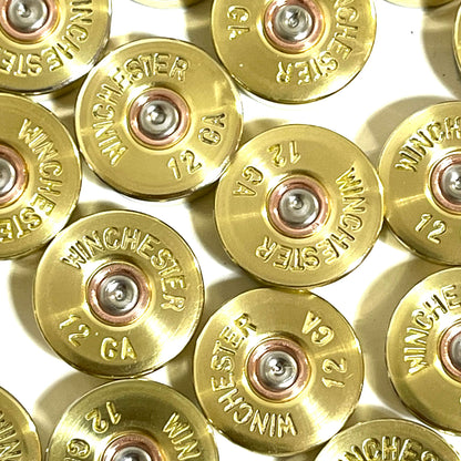 Close-up of gold brass shell heads with "Winchester 12 GA" headstamp text on a white background