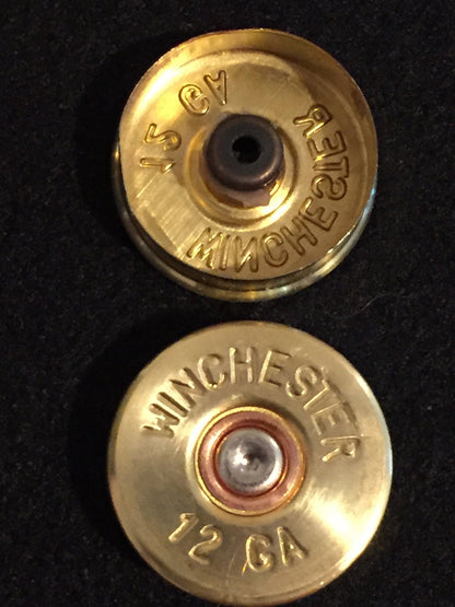 2 gold brass shell heads stacked, top showing a hollow primer pocket and bottom showing an intact "Winchester 12 GA" headstamp with silver primer