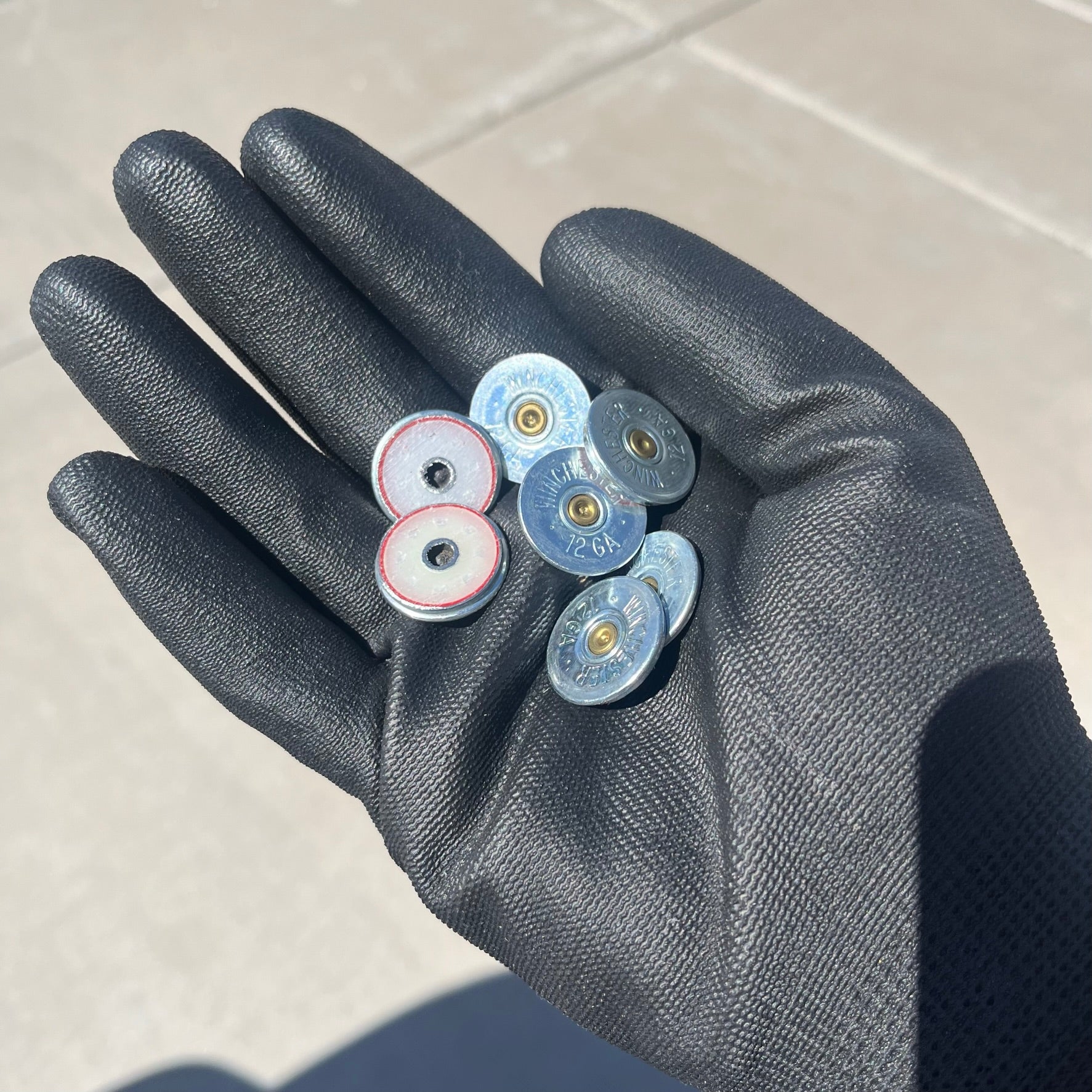Six silver Winchester shotgun shell slices held in a black gloved hand outdoors