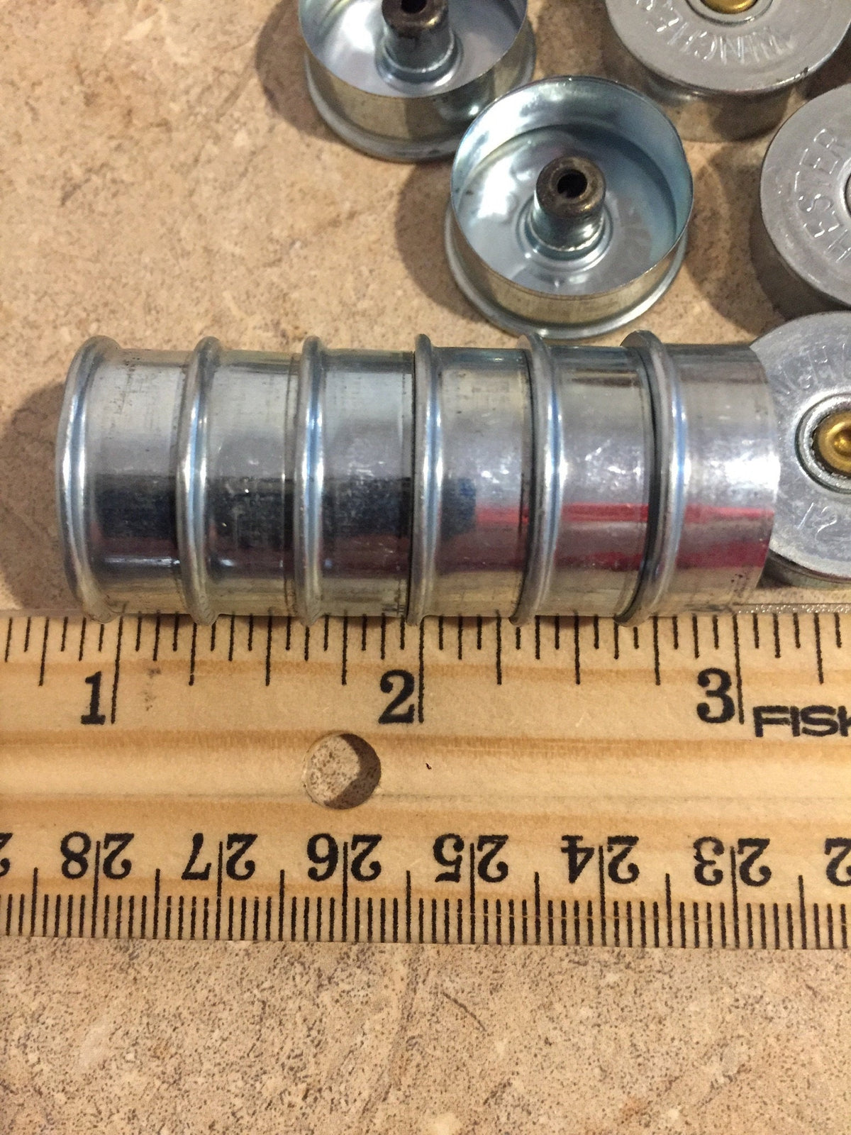 Silver Winchester 12 gauge steel headstamps nested and stacked, measured against a ruler showing a length of about 1.5 inches
