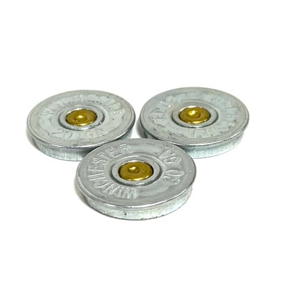 Three silver Winchester shotgun shell slices with brass primers on a white background
