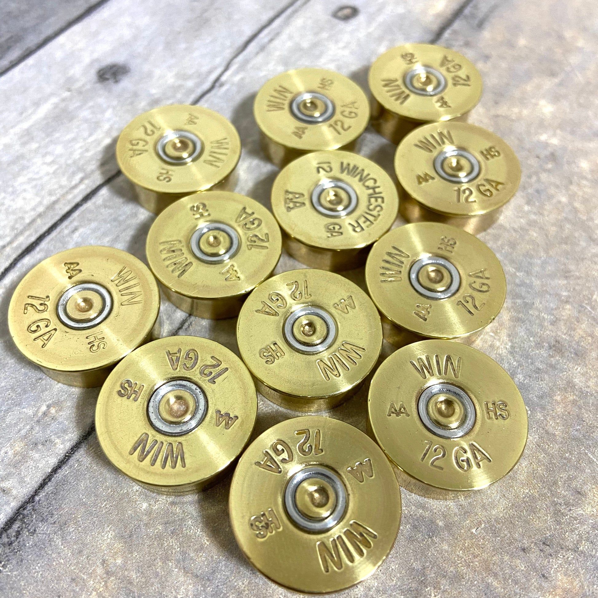 Twelve gold Winchester AA 12 gauge shotgun shell headstamps arranged on a wood-plank background, showing ‘WIN AA HS 12 GA’ stampings
