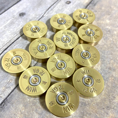 Twelve gold Winchester AA 12 gauge shotgun shell headstamps arranged on a wood-plank background, showing ‘WIN AA HS 12 GA’ stampings