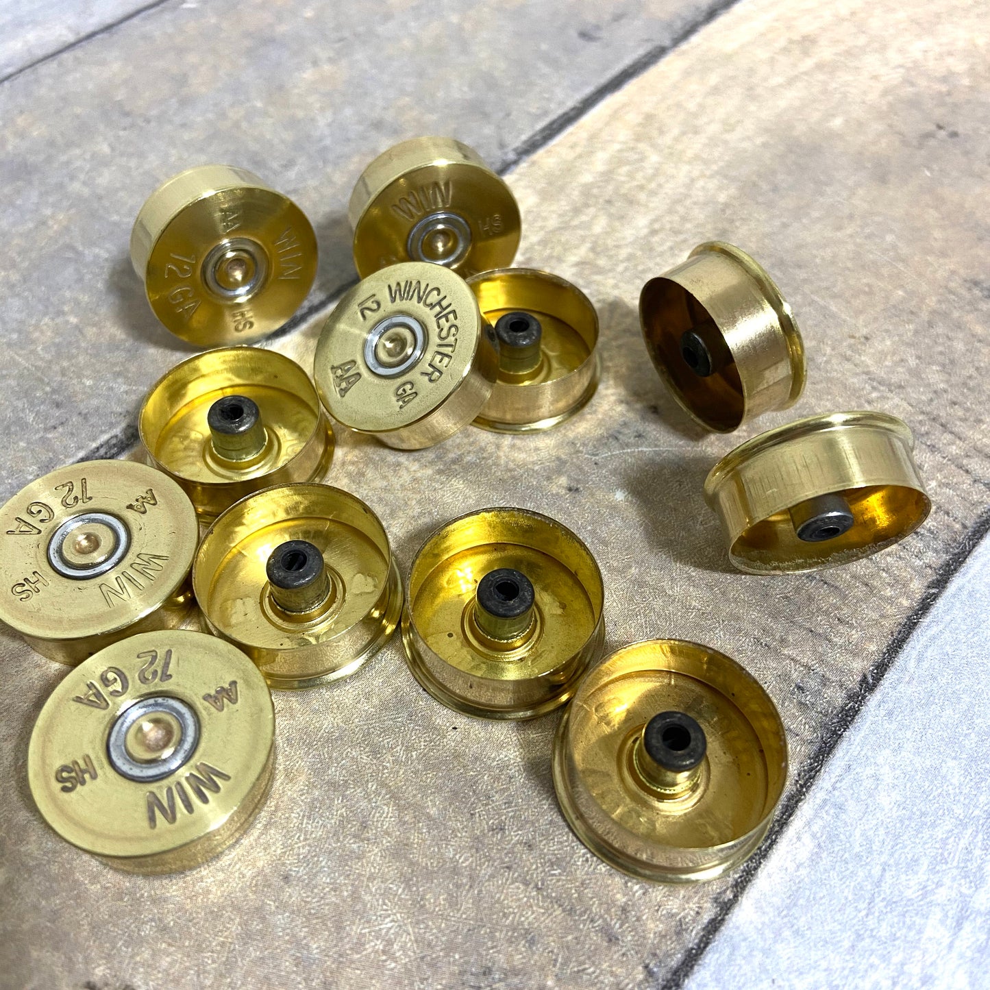 Gold Winchester AA 12 gauge shotgun shell headstamps viewed from underneath on a wood-plank background, showing spent primer pockets and hollow interiors