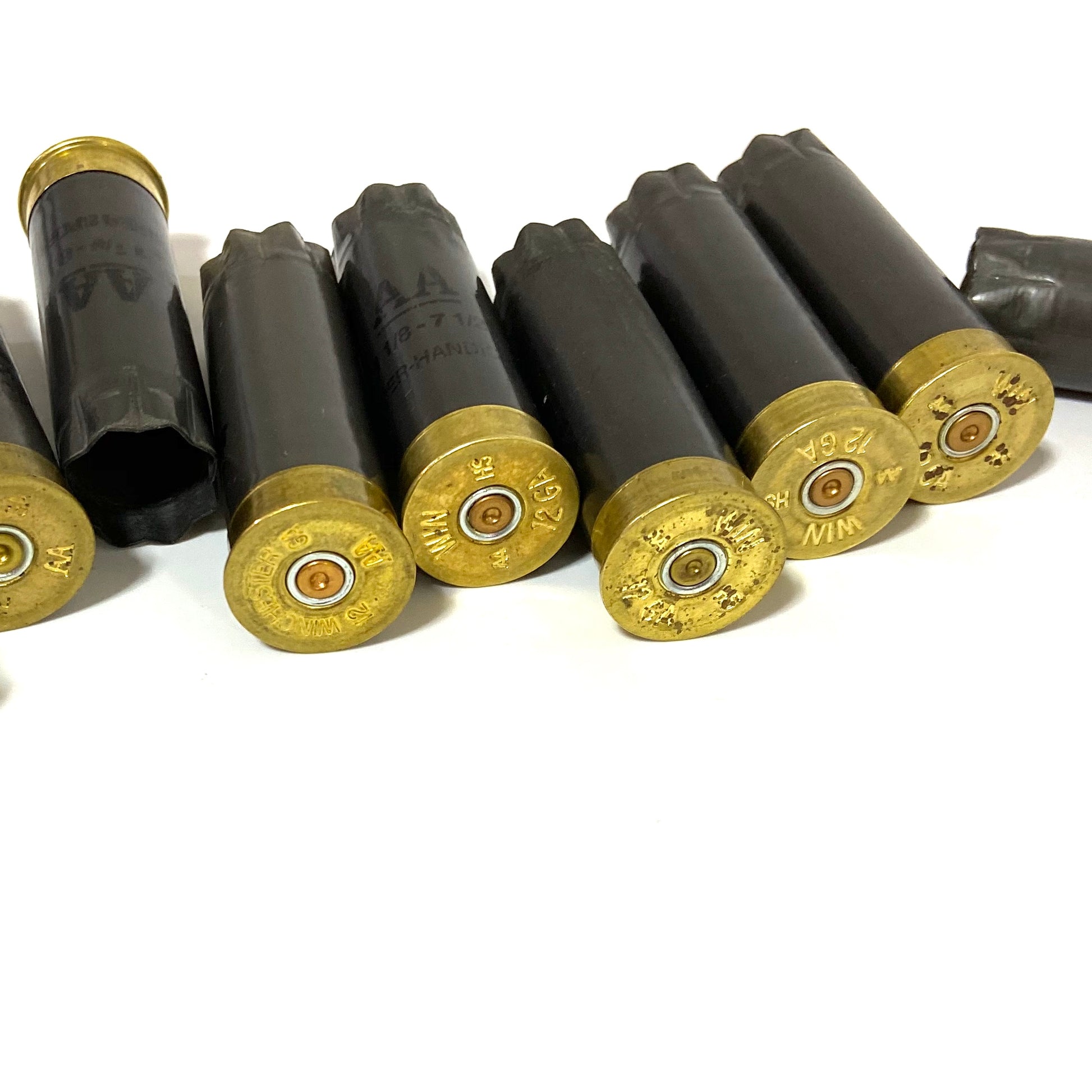 Seven spent gray Winchester AA 12 gauge shotgun shells on a white background with three showing brass headstamps.