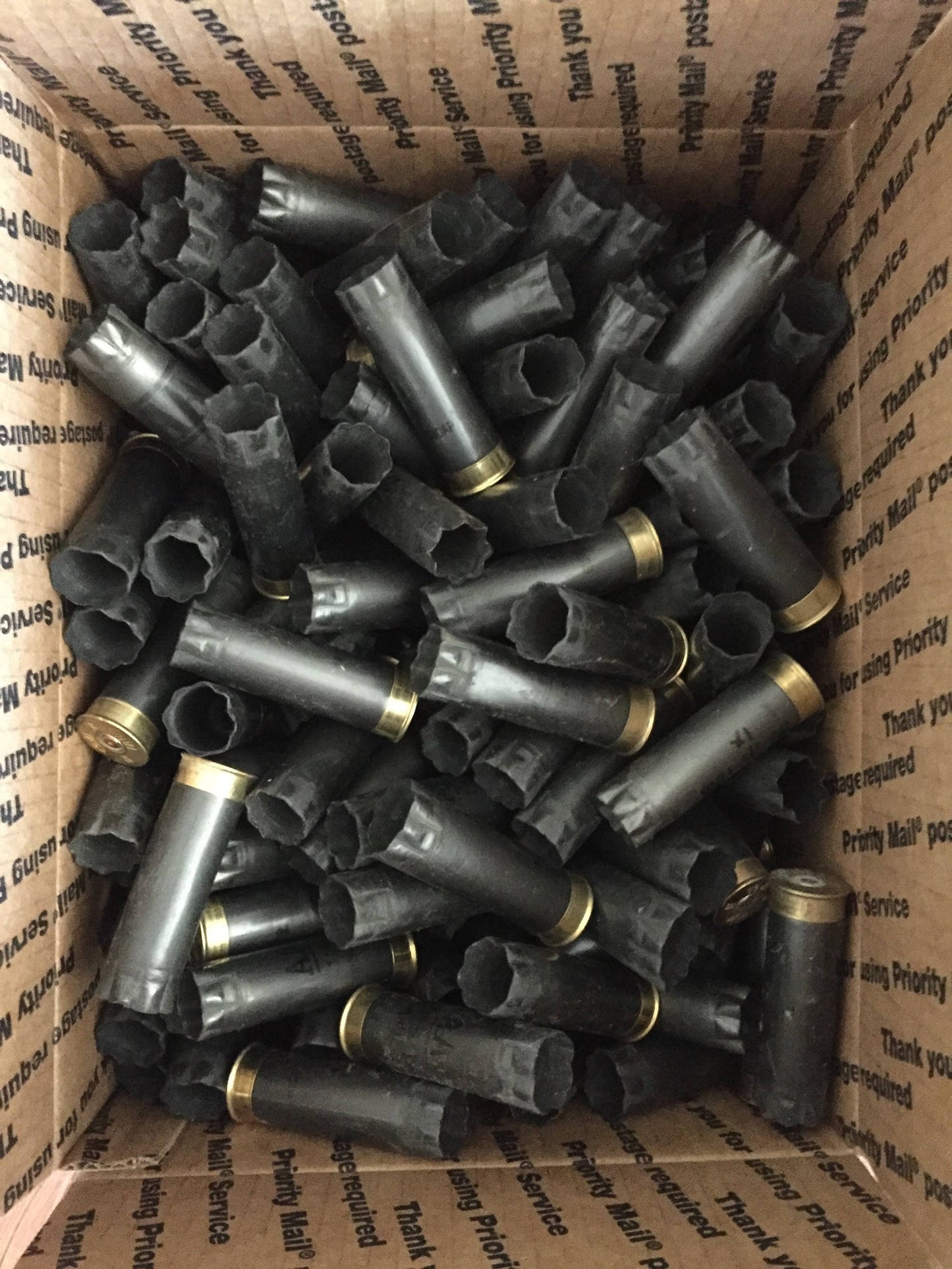 Bulk spent gray Winchester AA 12 gauge shotgun shells packed inside a USPS Priority Mail cardboard shipping box.