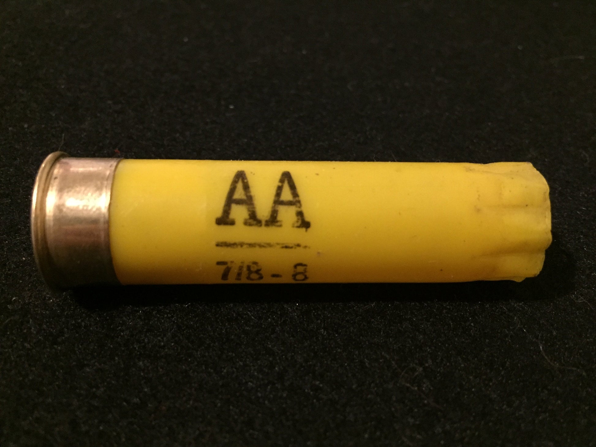 A single spent yellow casing lies on a dark textured background, marked 'AA 7/8-8'.