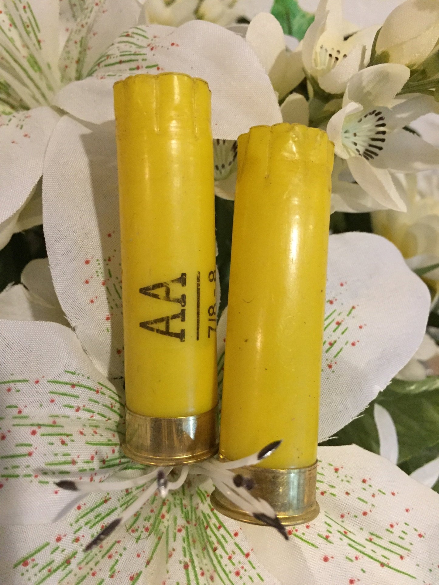 Two once-fired yellow cartridges nestled in white floral boutonniere greenery, one marked 'AA 7/8-8'.