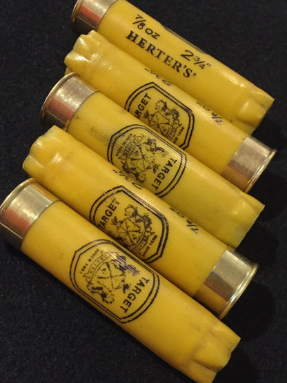 Yellow shotgun shell lying next to a wooden ruler showing its length