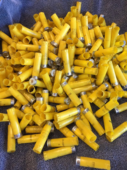 Large pile of yellow 20 gauge empty shotgun shells with silver bases on a gray cloth
