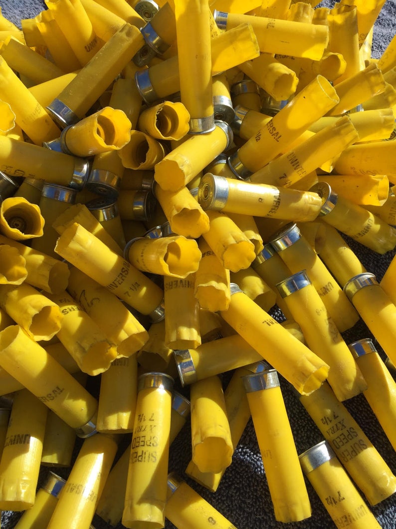 Large pile of yellow 20 gauge empty shotgun shells with silver bases in bright sunlight