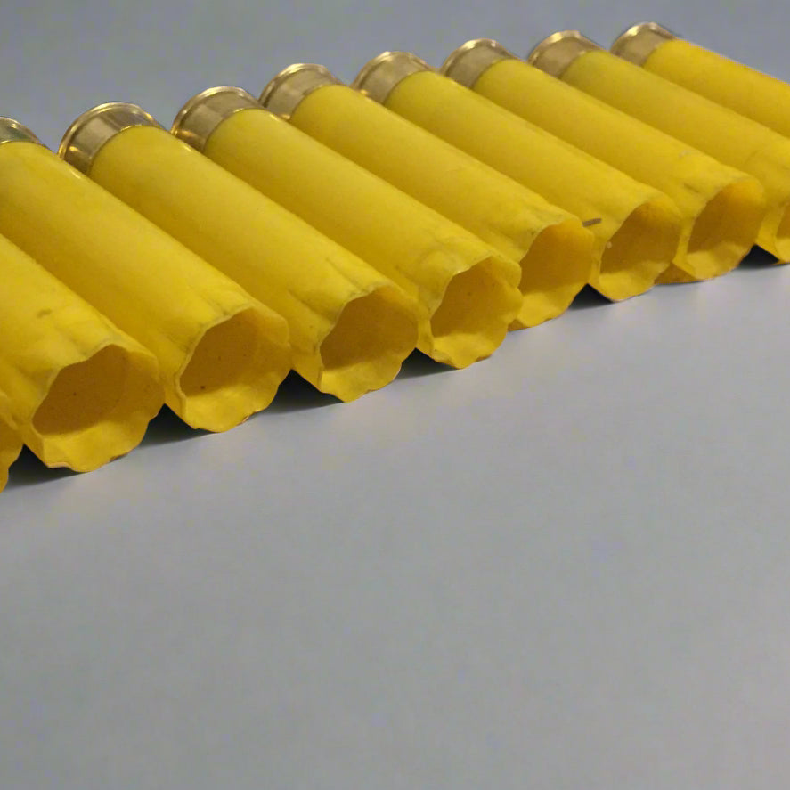 Row of yellow 20 gauge shotgun shell hulls viewed from the open end, showing the hollow interior