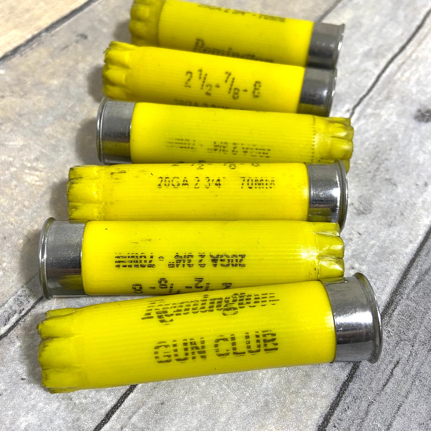 6 yellow Remington Gun Club shotgun shells lying diagonally across a wood-grain surface