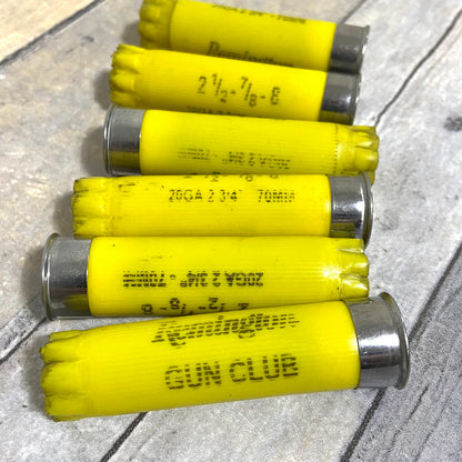 6 yellow Remington Gun Club shotgun shells lying diagonally across a wood-grain surface
