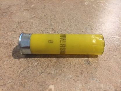 Single yellow 20 gauge empty shotgun shell with a silver base lying on a tile countertop