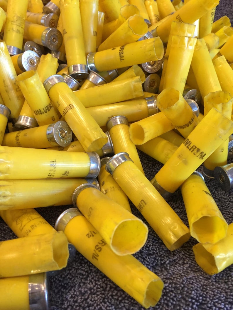 Large pile of yellow 20 gauge empty shotgun shells with silver bases on a dark speckled surface