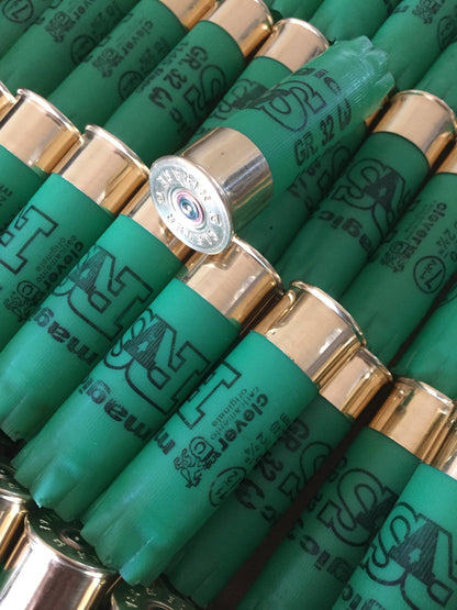 Rows of green shotgun shells with gold bases, one shell tilted showing a silver base with embossed headstamp text