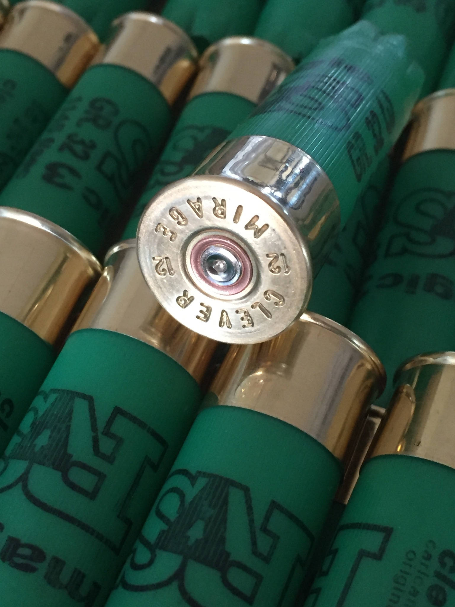 Close-up of a gold shotgun shell base embossed "Clever Mirage" surrounded by green shells printed "SAT magic"