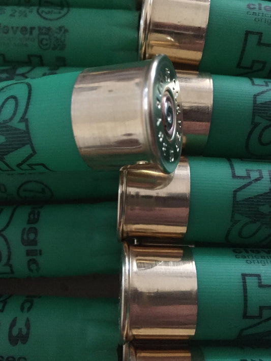 Close-up of a green shotgun shell silver base with embossed headstamp text, surrounded by other green shells